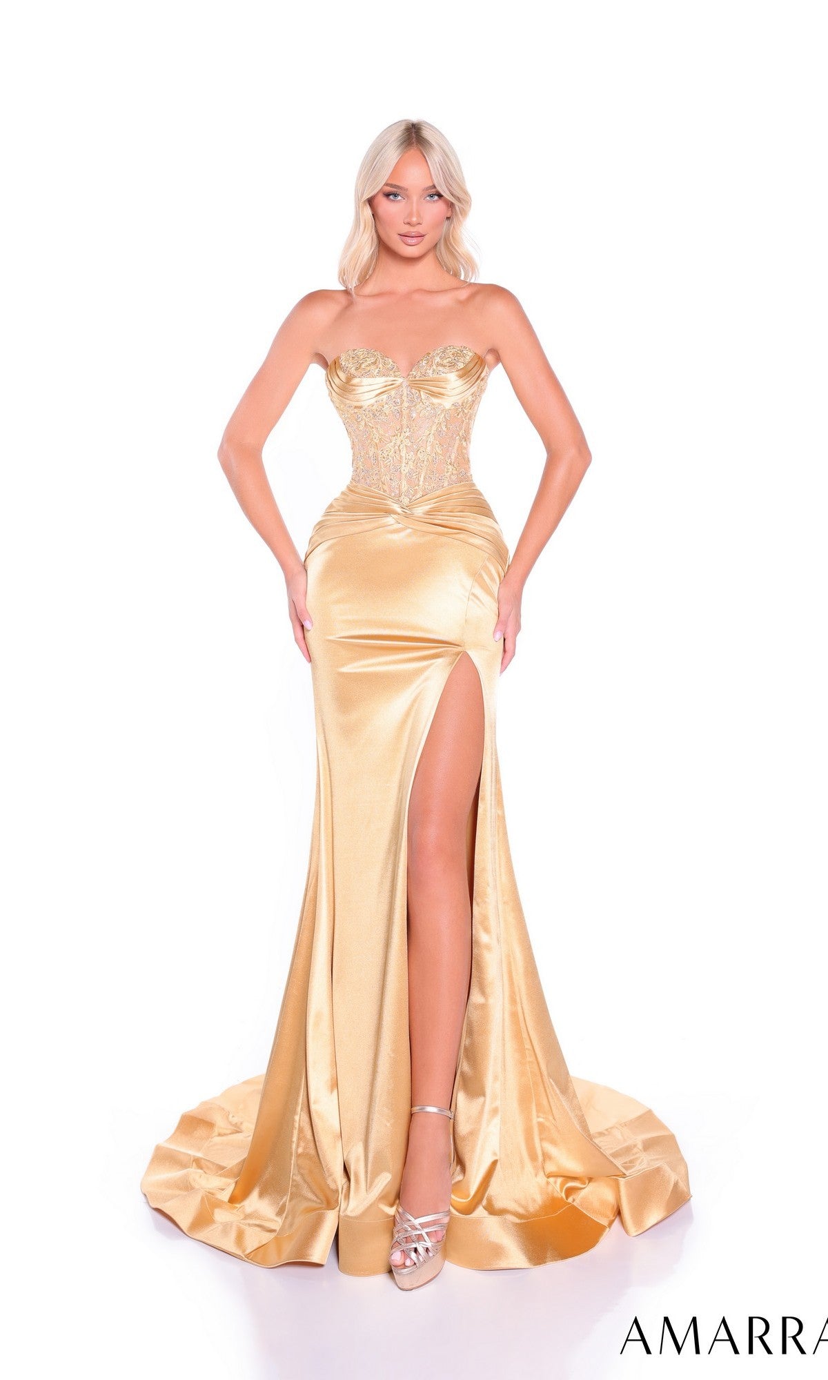 A woman wears the Amarra 89088 long gold prom dress featuring a strapless, high-leg slit design and a fitted, embellished lace corset bodice, standing against a white background.